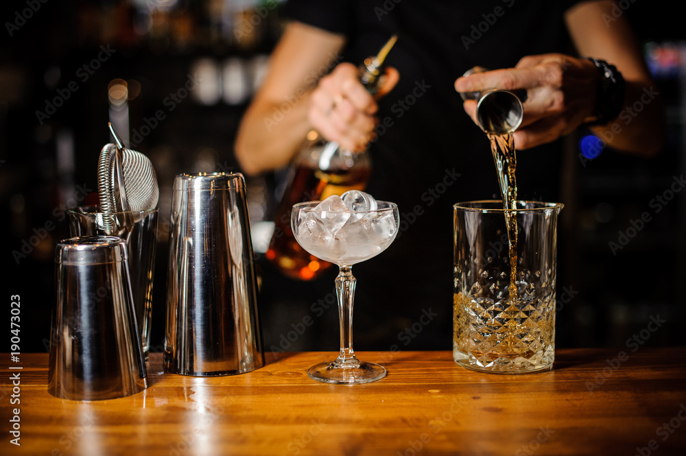 bartender prepares an amber-colored alcoholic cocktail using a crystal glass with ice