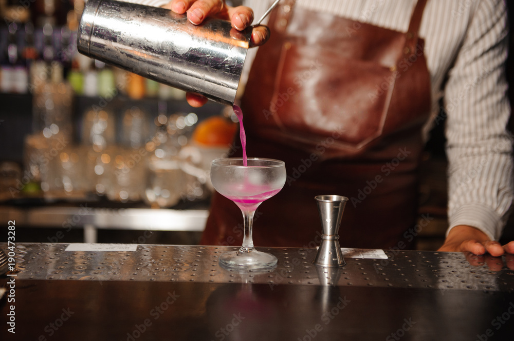 bartender pours from a steel shaker into a cocktail glass a lilac-colored alcohol cocktail bartender pours from a steel shaker into a cocktail glass a lilac-colored alcohol cocktail