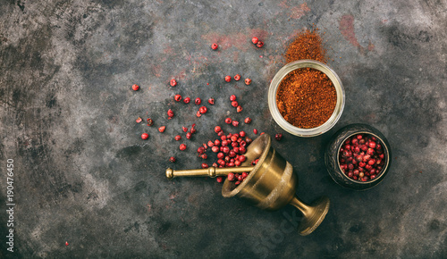 Pink peppercorns and powder and a bronze mortar on metal rusty background, top view, copy space