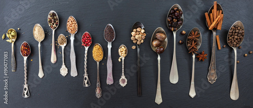 Fototapeta Naklejka Na Ścianę i Meble -  Variety of colorful spices in spoons on black stone background, top view, banner