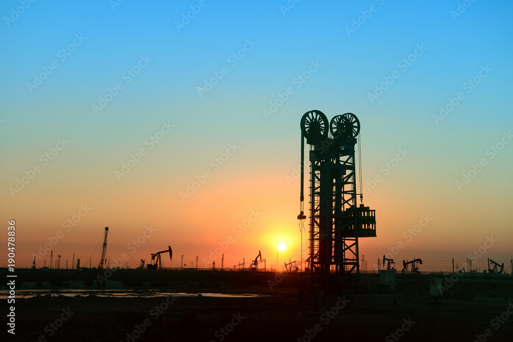Working oil derrick in field under the setting sun