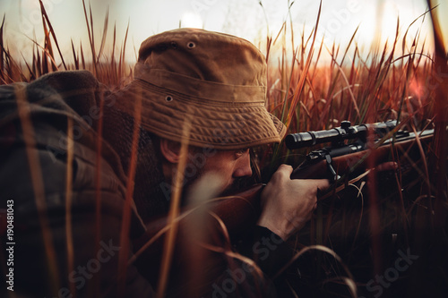 Hunter laying in long red grass looking trough his sniper photo