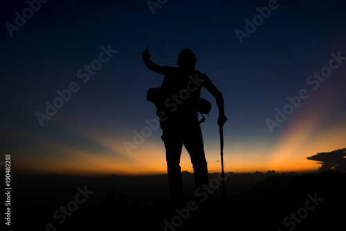 Silhouette of man hiking on top mountain trees forest with light during sunset, winter season