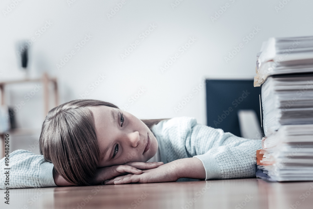 Nostalgic mood. Thoughtful little girl leaning on a table and concentrating on a pile of documents while thinking of something unpleasant and dreaming. Nostalgic mood. Thoughtful little girl leaning on a table and concentrating on a pile of documents while thinking of something unpleasant and dreaming.