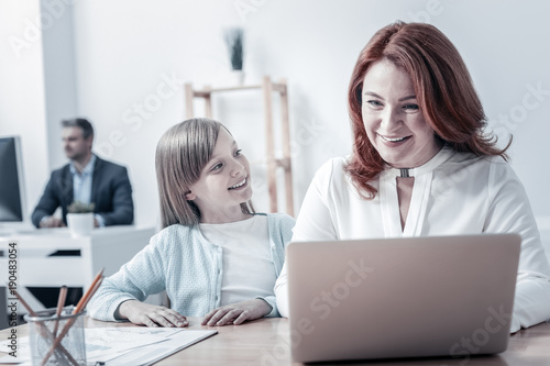 Wallpaper Mural Pleasant day. Joyful mature woman smiling while working on a laptop and listening to the questions of her curious little daughter. Torontodigital.ca