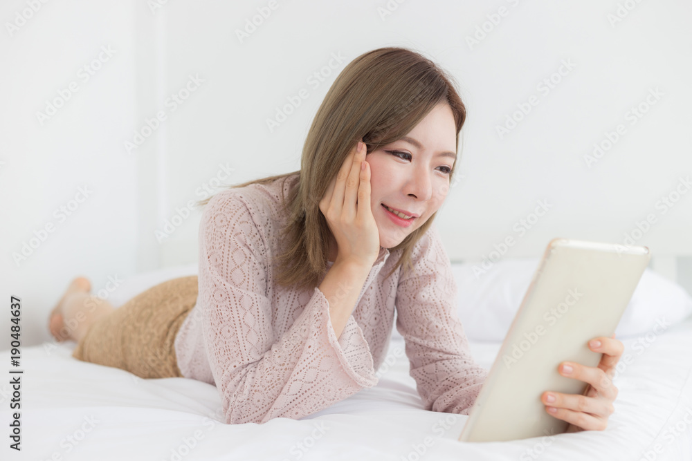 Happy Asian woman Smile and looking in tablet in bedroom Happy Asian woman Smile and looking in tablet in bedroom