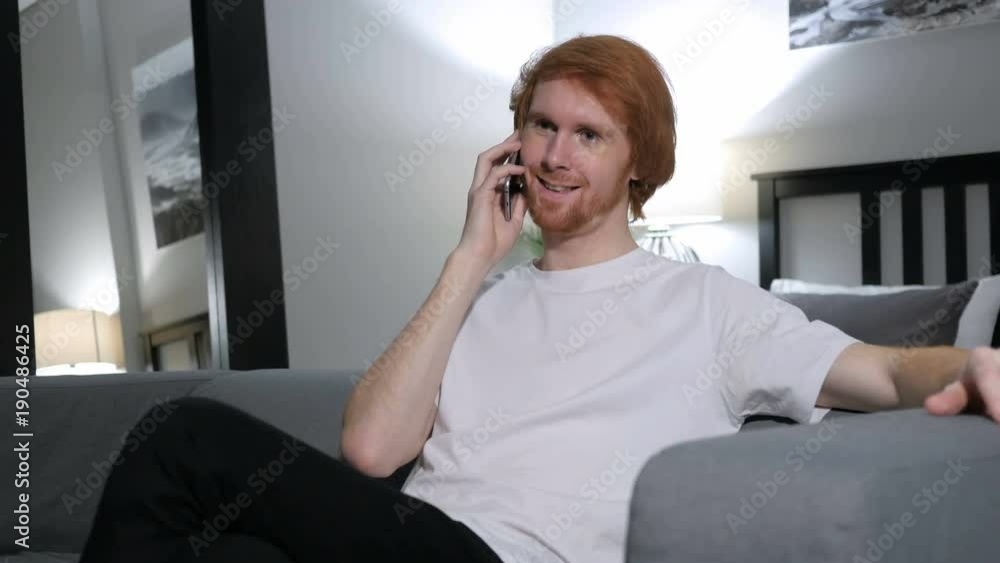 Redhead Man Talking on Phone, Sitting on Couch in Bedroom Redhead Man Talking on Phone, Sitting on Couch in Bedroom