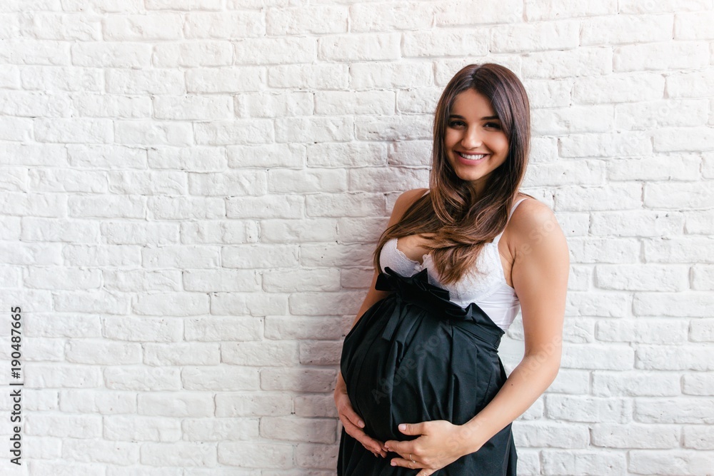 Pregnant young woman in a black skirt standing on white background holding belly hands Pregnant young woman in a black skirt standing on white background holding belly hands