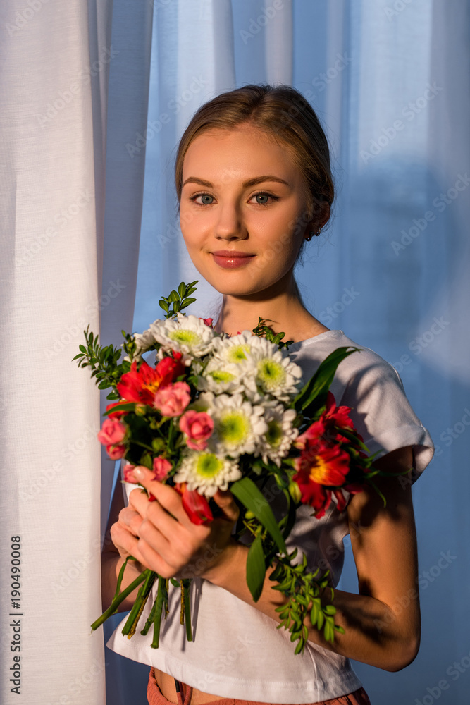 young woman with beautiful bouquet looking at camera against window