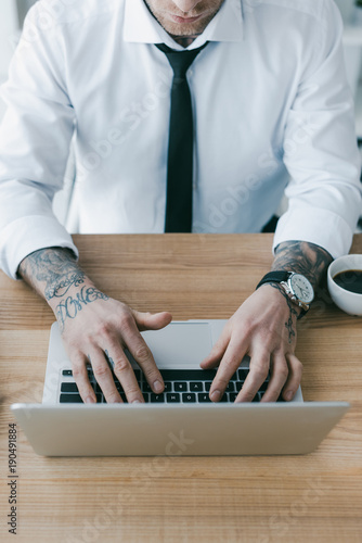 cropped shot of businessman with tattoos using laptop at workplace