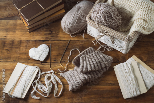 Light gray Knits in a basket and knitting needles, a white knitted scarf, a heart. Set with white ribbons on a wooden background. The concept of handmade. Flat lay, top view