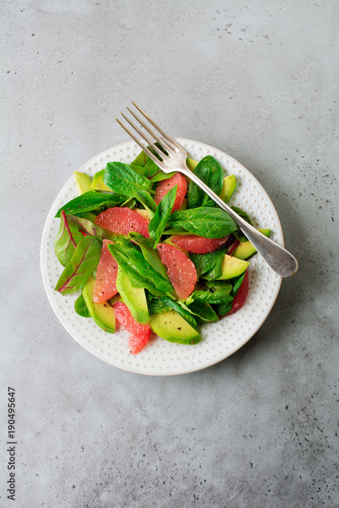 Useful tasty salad of spinach, chard, avocado and grapefruit with olive oil on old concrete gray background. Selective focus. Top view. Copy space. Useful tasty salad of spinach, chard, avocado and grapefruit with olive oil on old concrete gray background. Selective focus. Top view. Copy space.