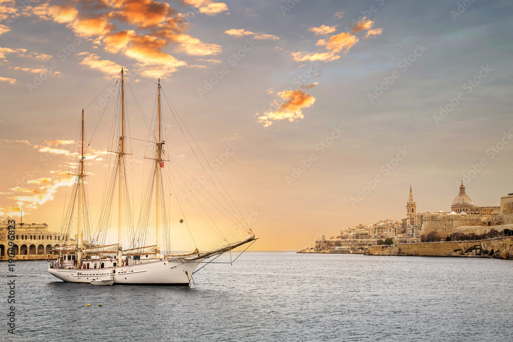Obraz premium Sunset with a yacht in Valletta, capital city of Malta, known in Maltese as Il-Belt. Scenic city view from the bay with a ship in front.