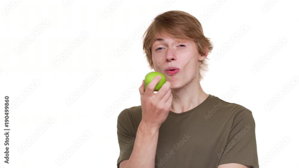 Portrait of joyous man in green t-shirt eating big green apple tasting juicy fruit enjoying food over white background. Concept of emotions Portrait of joyous man in green t-shirt eating big green apple tasting juicy fruit enjoying food over white background. Concept of emotions