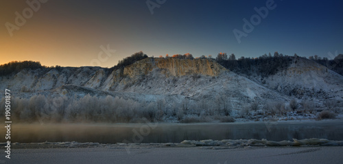 Winter frosty morning before dawn. Freezing river from the hilly banks and large ice floes.