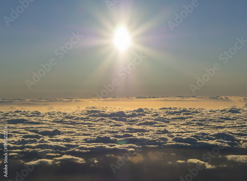 Bright early morning sun rising above the white orange fluffy clouds with sunbeam rays nad lens flare, nature abstract sunrise background