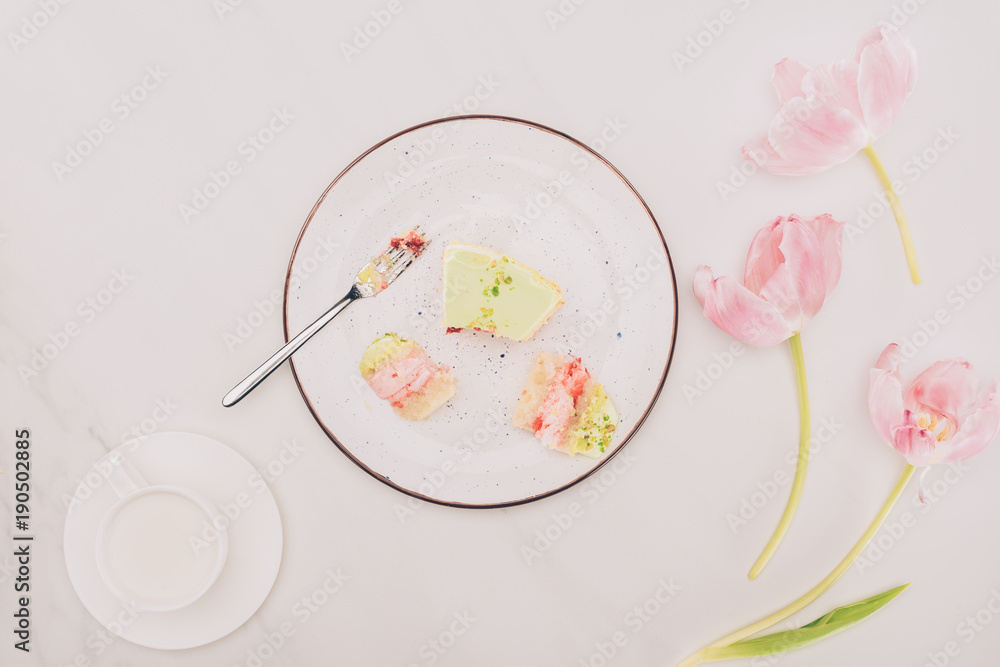 top view of pieces of cake on plate with fork, flowers and cup of milk on tabletop top view of pieces of cake on plate with fork, flowers and cup of milk on tabletop