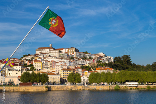 View on the old university city of Coimbra, the medieval capital of Portugal, from the river with Portuguese flag and the bridge. Popular touristic destination and attraction.