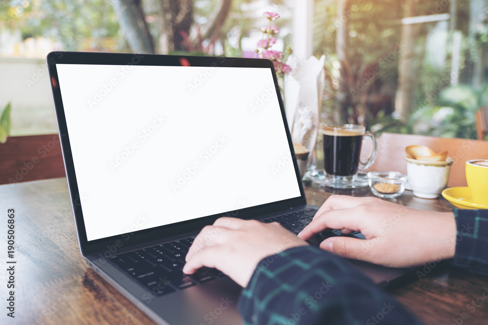 Mockup image of hands using and typing on laptop with blank white desktop screen on wooden table in cafe Mockup image of hands using and typing on laptop with blank white desktop screen on wooden table in cafe
