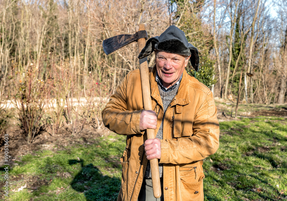Senior man with ax over his shoulder in the autumn garden.