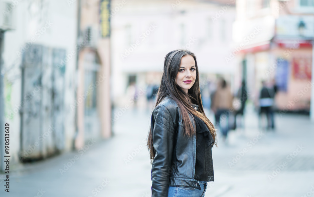 Closeup of an attractive young woman in her 20’s on a city street with out of focus stores and shoppers in the background. One man is looking at her. 