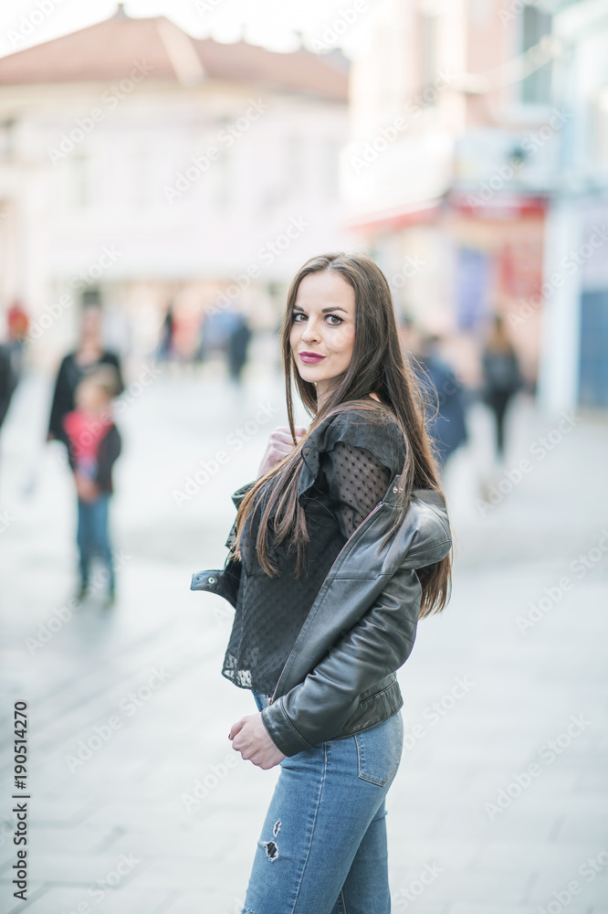 Modern attractive woman standing on a street close up portrait, woman touching hair, behind her are passers-by on the street, she enjoys life