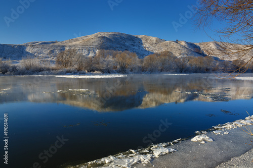 Freezing river from the hilly banks and large ice floes. A sunny day with a cloudless sky.