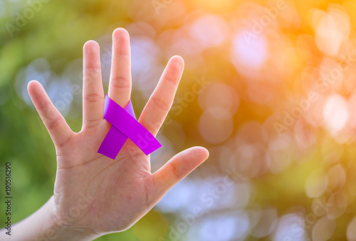  Cancer Awareness campaign. Female hands holding Purple CANCER awareness ribbon on green bokeh background..