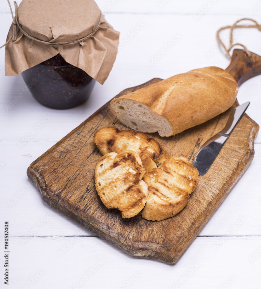 Naklejka premium pieces of white bread on a brown wooden board and raspberry jam