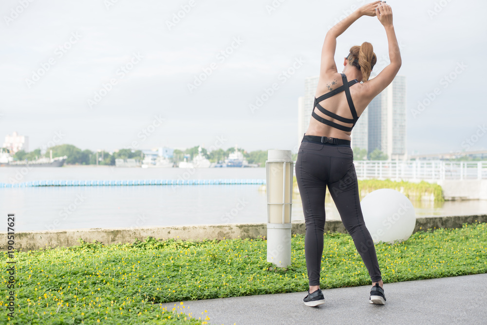 Fototapeta premium At the bsck asian woman doing stretching exercises outdoors along city sidewalk