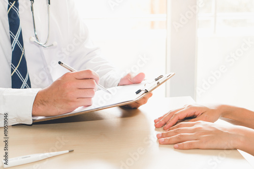 Close up hands of doctor taking note patient history to clipboard and giving diagnosis her disease. photo