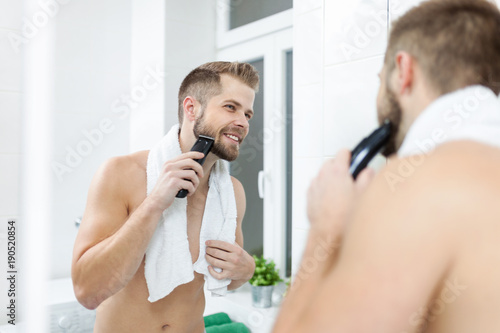 Handsome bearded man trimming his beard with a trimmer photo