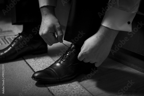 Bridegirl binds his shoes in black and white. a future husband tightens up for a wedding by putting on his shoes and tying his ties.