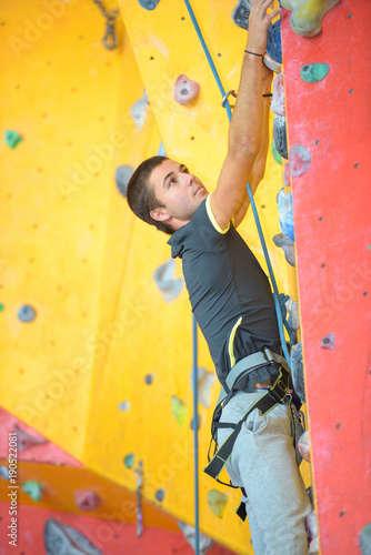 young man clibming indoor wall with safety rope