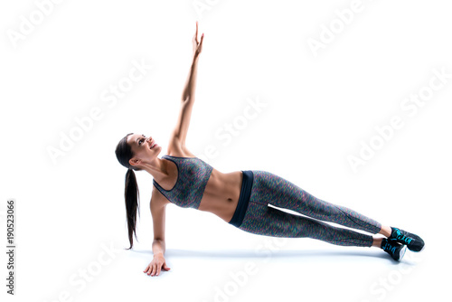 I want to feel like a million dollars! I do all my best to be healthy! Side profile view of purposeful attractive wearing tight pans and top sport woman doing plank, isolated on white background