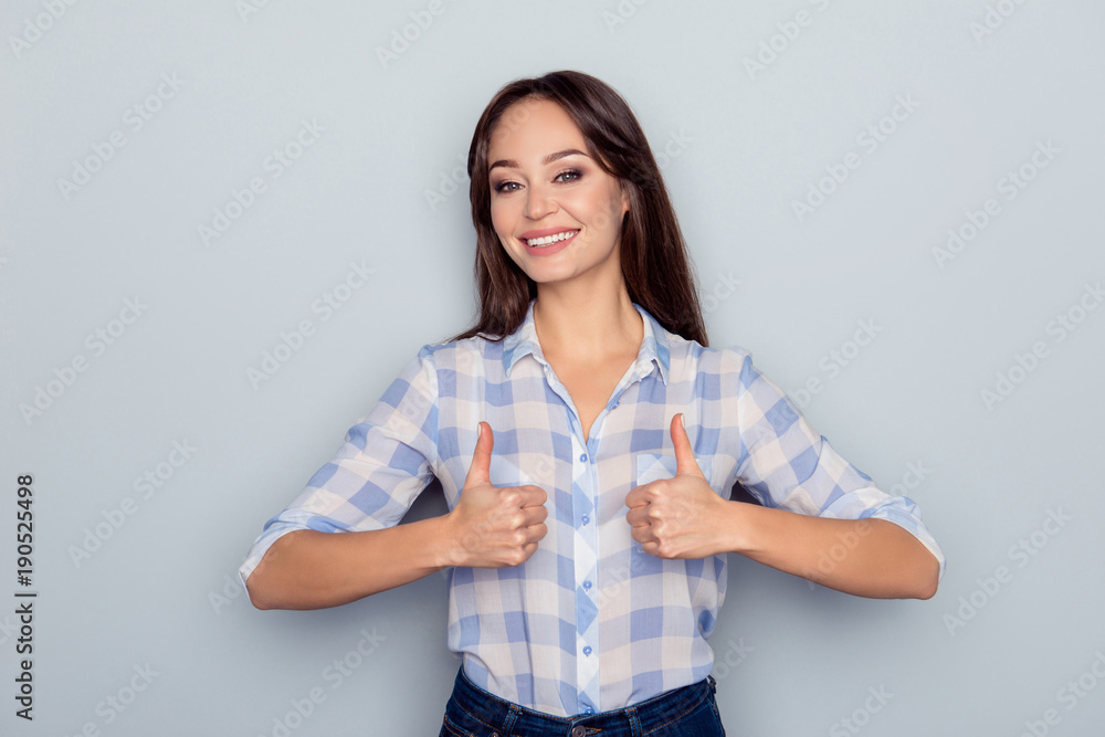 Portrait of gorgeous, cute, cheerful woman showing two thumbs up in checkered shirt over grey background Portrait of gorgeous, cute, cheerful woman showing two thumbs up in checkered shirt over grey background