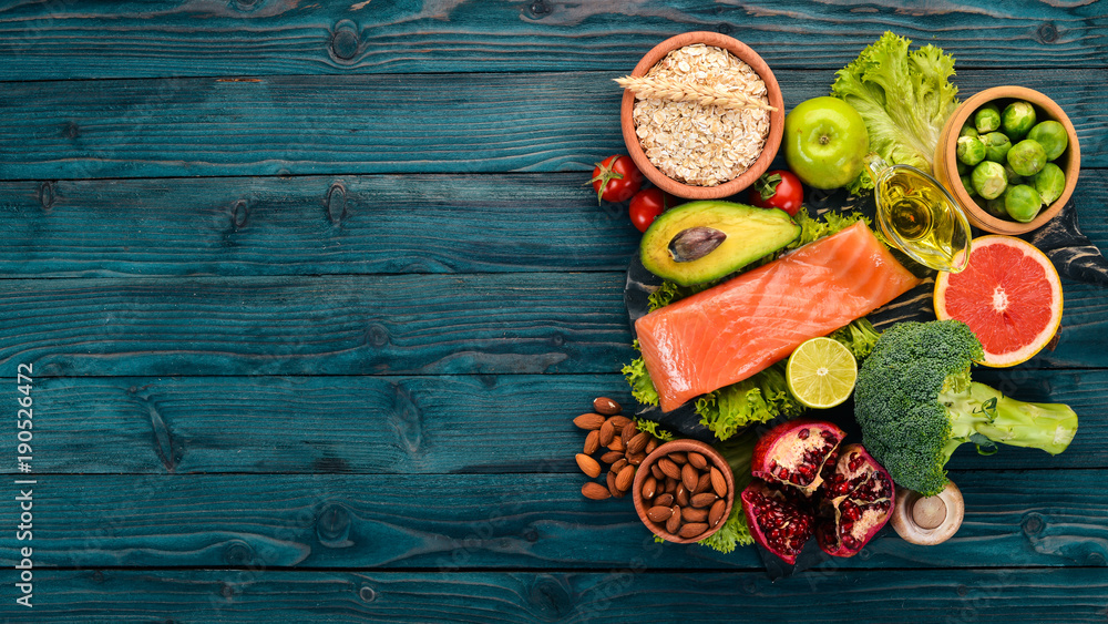 Healthy food. Fish salmon, avocado, broccoli, fresh vegetables, nuts and fruits. On a wooden background. Top view. Copy space. - obrazy, fototapety, plakaty 