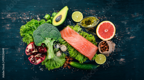 Healthy food. Fish salmon, avocado, broccoli, fresh vegetables, nuts and fruits. On a black background. Top view. Copy space.