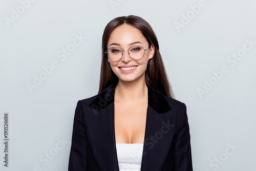 Portrait of young, caucasian, stunning, nice stylish, sexy woman in black jacket, formal wear  and beaming smile standing over grey background