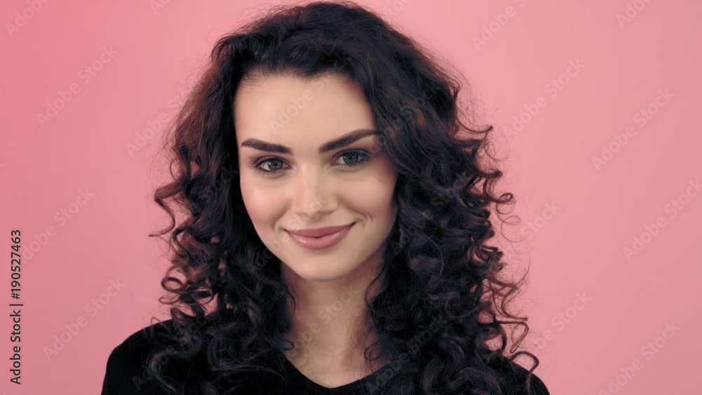 Beautiful fashionable girl with long curly hair in a black T-shirt. Girl in the studio on a pink background.Advertising, hair products, beauty salon, cosmetics, clothing. Fashion, boutique. Pink. Beautiful fashionable girl with long curly hair in a black T-shirt. Girl in the studio on a pink background.Advertising, hair products, beauty salon, cosmetics, clothing. Fashion, boutique. Pink.