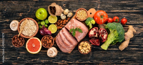 Healthy food. Raw meat, avocado, broccoli, fresh vegetables, nuts and fruits. On a wooden background. Top view. Copy space.
