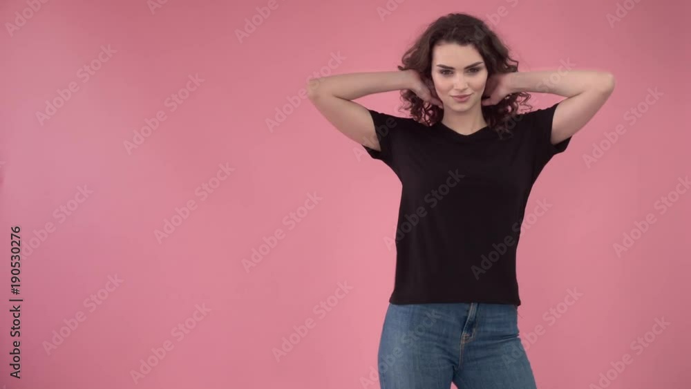 Beautiful fashionable girl with long curly hair in a black T-shirt. Girl in the studio on a pink background.Advertising, hair products, beauty salon, cosmetics, clothing. Fashion, boutique. Pink. Beautiful fashionable girl with long curly hair in a black T-shirt. Girl in the studio on a pink background.Advertising, hair products, beauty salon, cosmetics, clothing. Fashion, boutique. Pink.