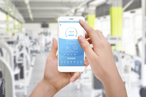 Female person using fitness application on her phone, gym in background. Fitness technology concept