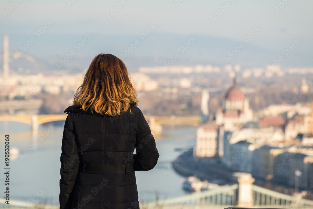 Young woman is looking at the Budapest parliament building and Chain bridge from Citadel on the top of Gellert Hill in Budapest, Hungary.