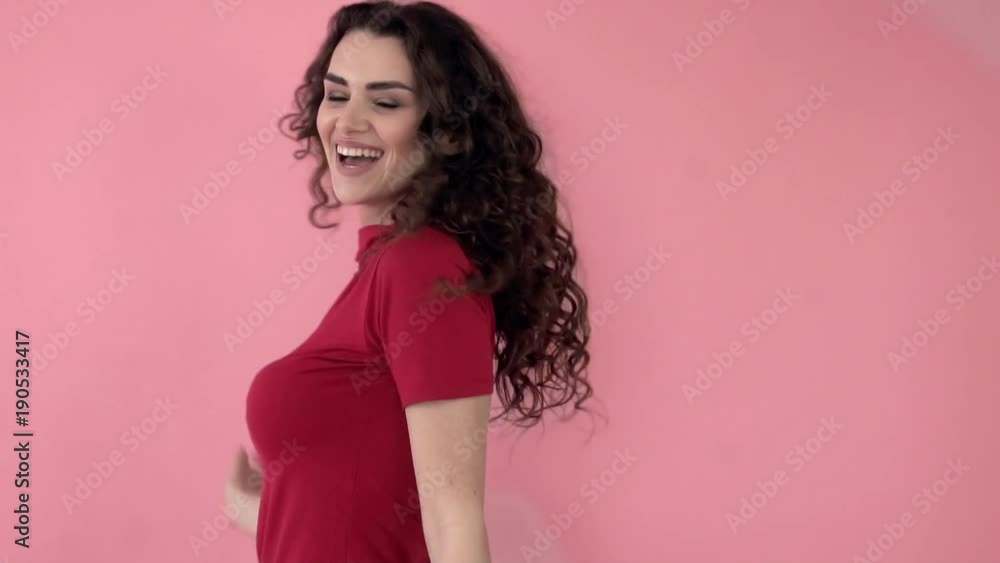 Beautiful fashionable girl with long curly hair in a red T-shirt. Girl in the studio on a pink background.Advertising, hair products, beauty salon, cosmetics, clothing. Fashion, boutique. Pink. Beautiful fashionable girl with long curly hair in a red T-shirt. Girl in the studio on a pink background.Advertising, hair products, beauty salon, cosmetics, clothing. Fashion, boutique. Pink.