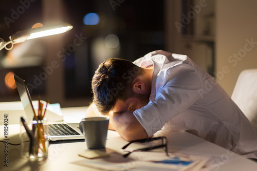 tired businessman lying on table at night office photo