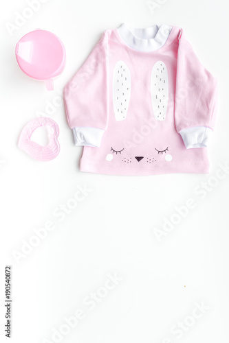 Cute pink baby clothes for girl. Shirt, toy, bottle on white background top view copy space