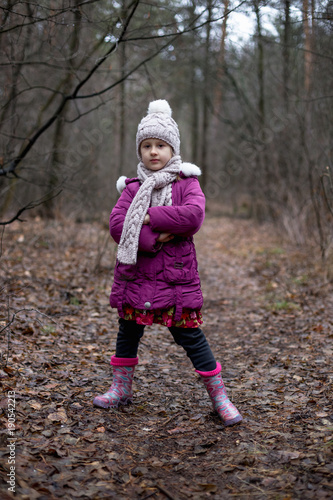 A little girl is standing in a forest on a path.