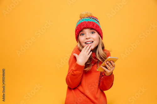 Confused Young girl in sweater and hat holding smartphone