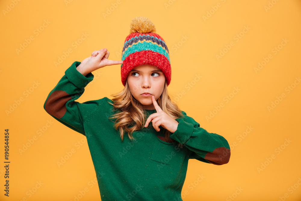 Serious girl in sweater and hat with fingers on temple Serious girl in sweater and hat with fingers on temple